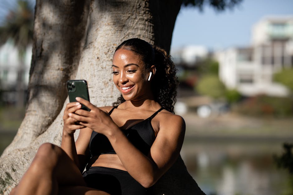 Why Neck Humps Are Common in Women in Their 20s–30s A happy woman sitting under a tree, texting on her smartphone while enjoying the sunny outdoors.